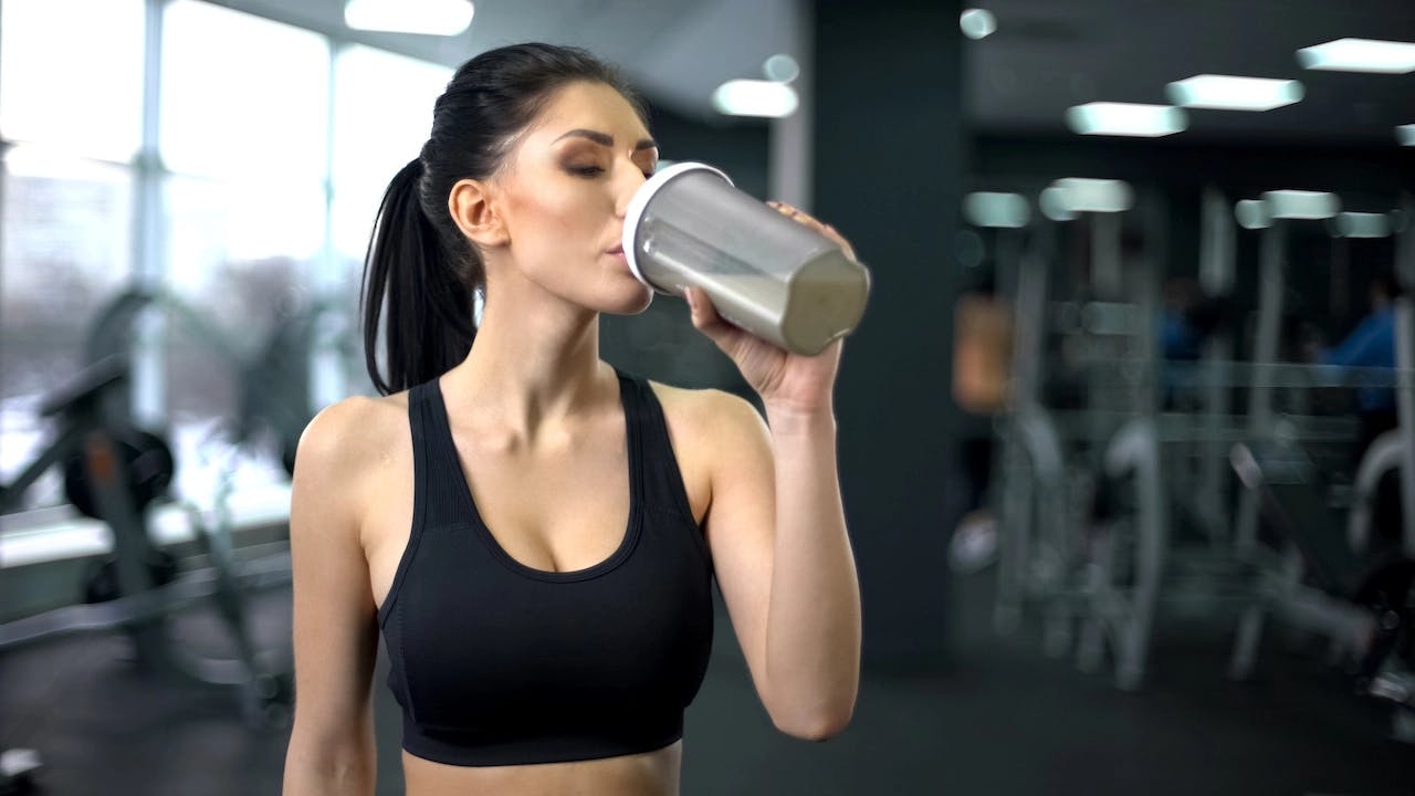 une femme boit dans une gourde une boisson protéinée